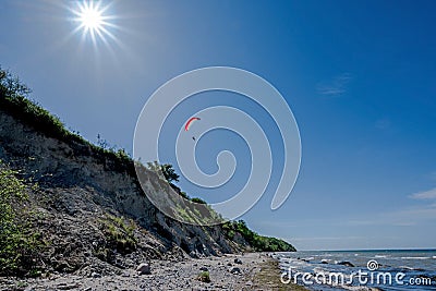 Paraglider is flying over the steep coast on the beach of the Baltic Sea, beautiful landscape for outdoor sports, blue sky with Stock Photo