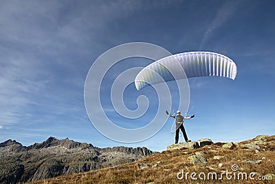 Paraglider pilot stands on a rock and balances his paraglider above his head near Lake Grimsel in the Swiss Alps Stock Photo