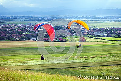 Paragliders flying over green fields Stock Photo