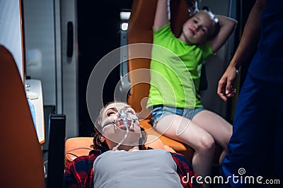 Paramedic puts oxygen mask on woman liyng on stretcher in the ambulance car Stock Photo