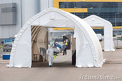 Paramedic wearing protective equipment disinfecting mobile testing station tent for cars Editorial Stock Photo