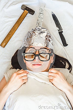 Paranoid girl wears foil hat and sleeps with weapon and different glasses because of mental disorder Stock Photo