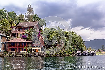 Guest houses in the form of a traditional Indonesian dwelling with a pier for boats on the Editorial Stock Photo