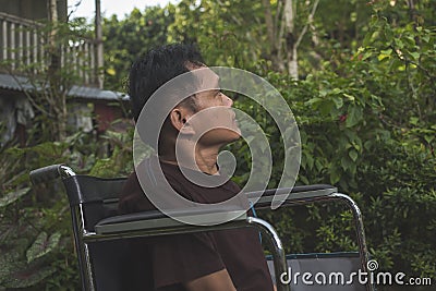 A paraplegic middle aged man in his wheelchair stares blankly while outside his home. A bored and lonely person Stock Photo