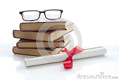 A parchment diploma scroll, rolled up with red ribbon beside a stack of books on white background. Stock Photo