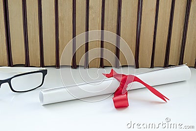 A parchment diploma scroll, rolled up with red ribbon beside a stack of books on white background. Stock Photo