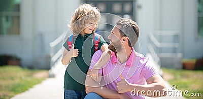 Parent and pupil of primary school with thumbs up sign. Teacher in t-shirt and cute schoolboy with backpack near school Stock Photo