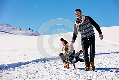 Parenthood, fashion, season and people concept - happy family with child on sled walking in winter outdoors Stock Photo