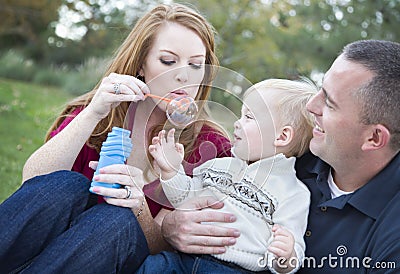 Parents Blowing Bubbles with their Child in Park Stock Photo