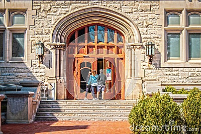 Parents and female student entering large arched doors of University building flanked by metal gothic lamps Editorial Stock Photo