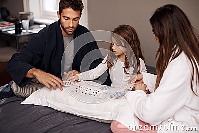 Parents, girl and fun with playing cards for game for bonding, learning and relax with strategy in bedroom. Father Stock Photo