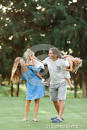 Parents Giving Children Piggybacks In Countryside enjoing time together. Happy family concept. Blurred trees background Stock Photo