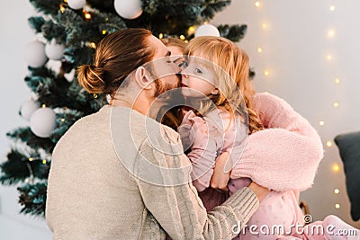 Parents hug and kiss their beloved daughter. Young family in a Christmas decorated room. Stock Photo