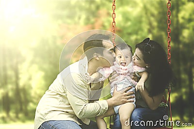 Parents kiss their child on swing Stock Photo