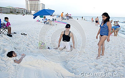 Parents looking at their daughter after they have sculpted her into a mermaid in the sand Editorial Stock Photo