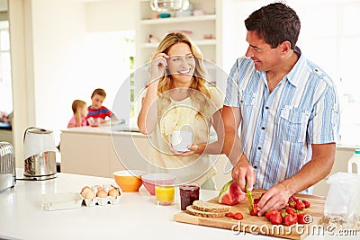 Parents Preparing Family Breakfast In Kitchen Stock Photo