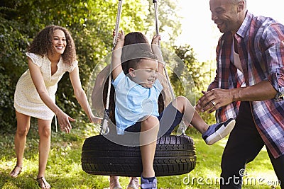 Parents Pushing Children On Tire Swing In Garden Stock Photo