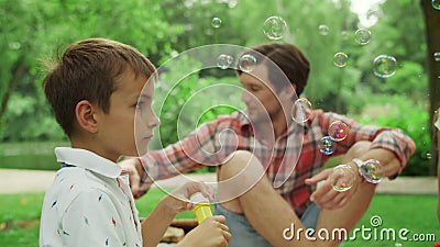 Parents relaxing on blanket in park with kids. Children blowing soap bubbles Stock Photo