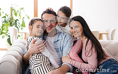 Parents with small daughters sitting on sofa indoors at home, looking at camera. Stock Photo