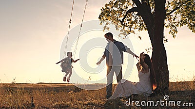 Parents swing a happy child high up on a swing at sunset, a cheerful family in the glare of the sun plays with their Stock Photo