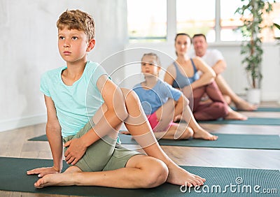 Parents together with children practice yoga in Gomukhasana pose in gym Stock Photo