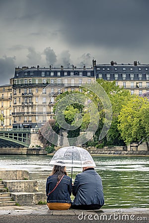 2 people take shelter under their umbrella in the middle of summer in Paris along Seine River Editorial Stock Photo