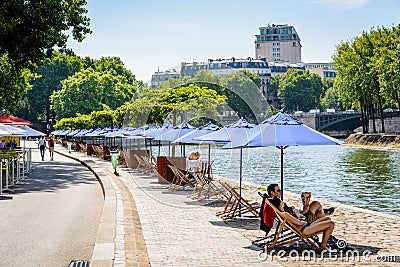 Row of parasols and deck chairs in the sun on the wharf of the river Seine Editorial Stock Photo