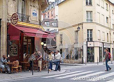 Urban street scene of people standing in group talking, one sitting at cafe and others walking. Editorial Stock Photo