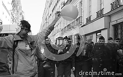 A protestor dressed up as a clown with a balloon stands next to French riot police Editorial Stock Photo