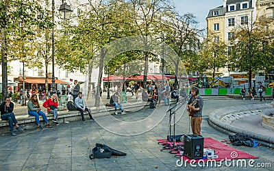 A musicians entertains young people sitting around a fountain Paris, France Editorial Stock Photo