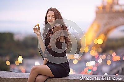 Paris woman smiling eating the french pastry macaron in Paris against Eiffel tower. Stock Photo