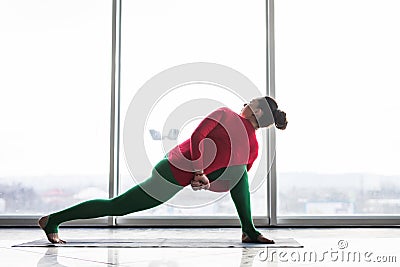 Parivritta parsvakonasana. Beautiful yoga woman practice twist poses in a big window hall Stock Photo