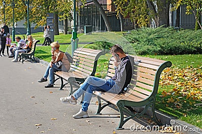 In the park on a bench a guy and a girl are talking on the phone. Editorial Stock Photo