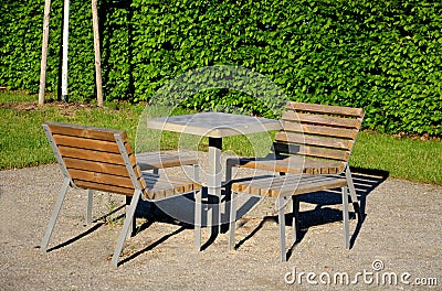 Park furniture chess table and chairs for four persons made of light metal and wooden beams with backrest on bright glade area gra Stock Photo