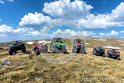 Parked ATV and UTV, buggies on mountain peak with clouds and blue sky in background Stock Photo