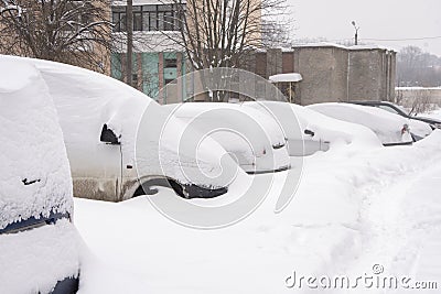 Parked cars, covered in snow, stand along the road. Snowfall in the city, falling snowflakes. Concept: traffic collapse, increased Stock Photo