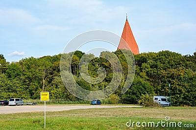 Parking lot with cars and town sign in Kirchdorf, Insel Poel, Germany with church roof behind the trees Editorial Stock Photo