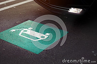 parking lot scene with car entering a section marked with symbol of a car with cable plug painted on ground. Stock Photo