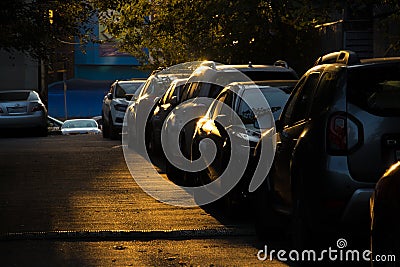 Parking. A row of cars in a parking lot lit by yellow sunlight in a dark, shady courtyard. Stock Photo