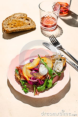 Parma ham, mozzarella and peaches sandwich on a plate, some bread and rose wine shot with hard light Stock Photo