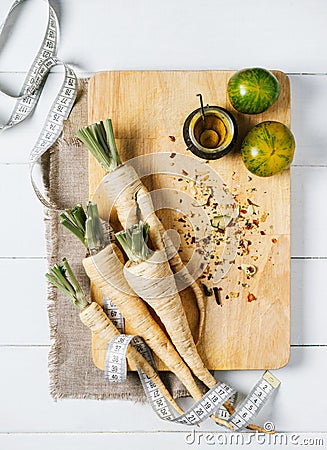 Parsley root with a measuring tape and tomatoes on cutting board on a white background of the old wooden boards vintage top view Stock Photo
