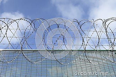 Part of a barbwired fence on a blue sky with clouds Stock Photo