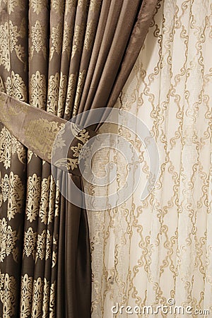 Part of beautifully draped curtain on the window in the room. Close up of piled curtain. Luxury curtain, home decor. Gold and brow Stock Photo