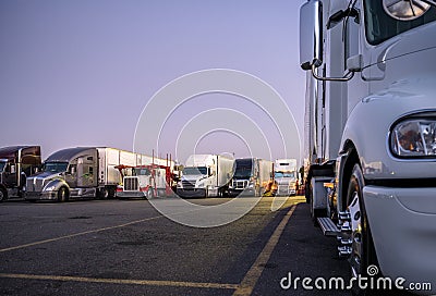 Part of big rig semi truck in front of another semi trucks standing in row on night truck stop parking lot in the headlights Stock Photo