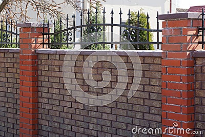 Part of a brown brick fence with black sharp iron rods Stock Photo