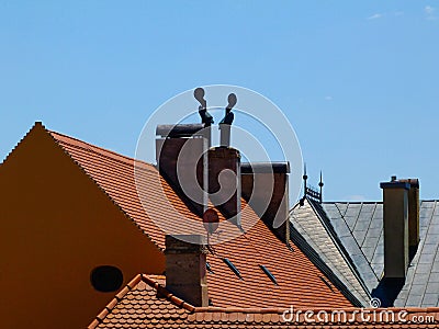 Part of clay tile roof structure and brick chimneys with concrete capping and metal wind vane. Stock Photo