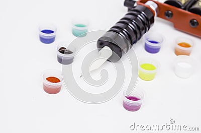 Part of the induction tattoo machine and colored paint in disposable plastic jars on a white background. Tattoo equipment. Side vi Stock Photo