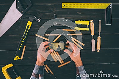 partial view of carpenter holding goggles in hands with various industrial tools around Stock Photo