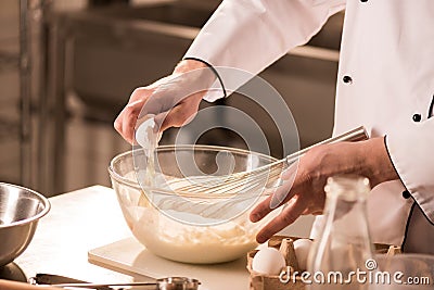 partial view of confectioner adding raw egg into dough Stock Photo