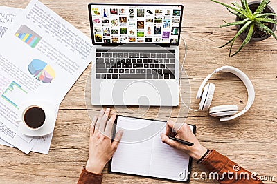 partial view of man making notes in notebook at workplace with laptop with pinterest website, papers, cup of coffee Editorial Stock Photo